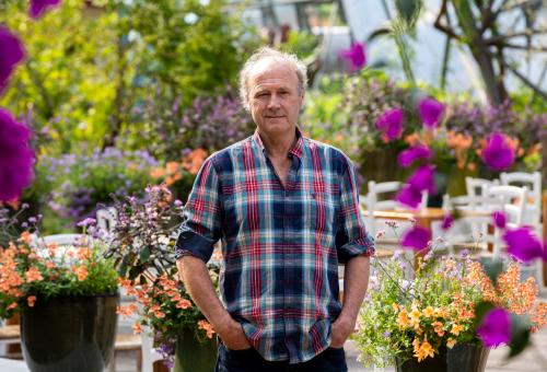 A picture of Sir Tim Smit in one of biomes surrounded by purple and orange flowers